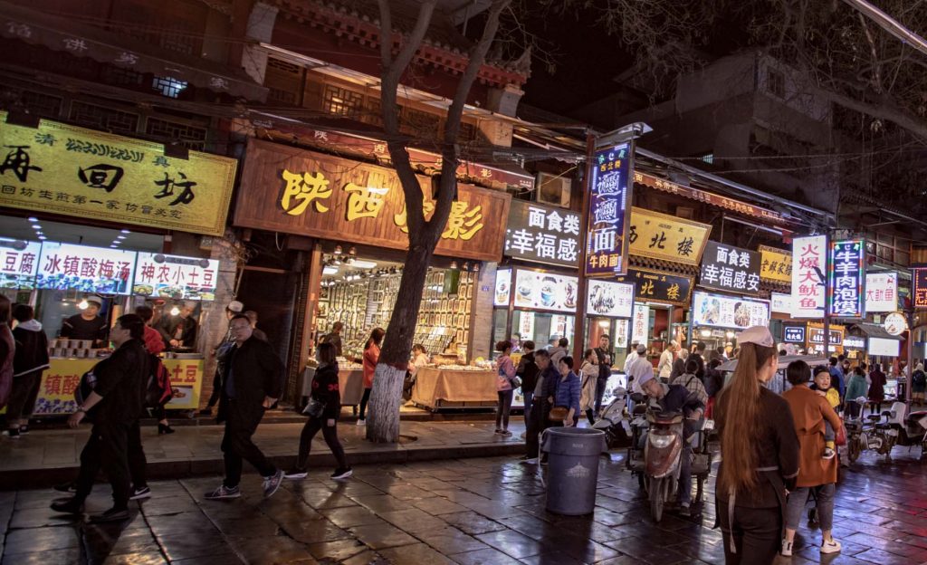 Crowded Chinese street food market at night with steam rising from food stalls and red lanterns overhead